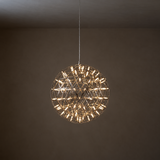 A spherical wire-frame pendant light with many small illuminated bulbs, hanging from a thin cord against a dark brown wall and ceiling.
