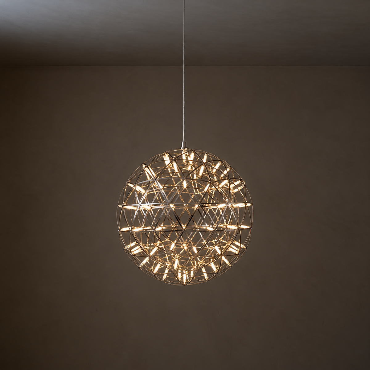 A spherical wire-frame pendant light with many small illuminated bulbs, hanging from a thin cord against a dark brown wall and ceiling.