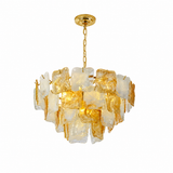 A modern chandelier featuring a gold-finished metal canopy and chain, with multiple irregular translucent amber and frosted glass pieces clustered in a circular shade, shown against a plain white background.