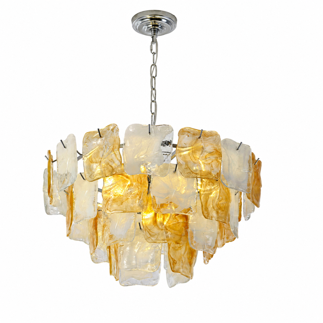 A modern chandelier featuring multiple irregular, translucent amber and frosted glass panels that glow warm when lit, suspended from a polished silver ceiling canopy by a chain.