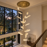 A modern multi-light chandelier with glowing, cloud-like leaf-shaped bulbs suspended from a round brass ceiling canopy in a contemporary home interior.