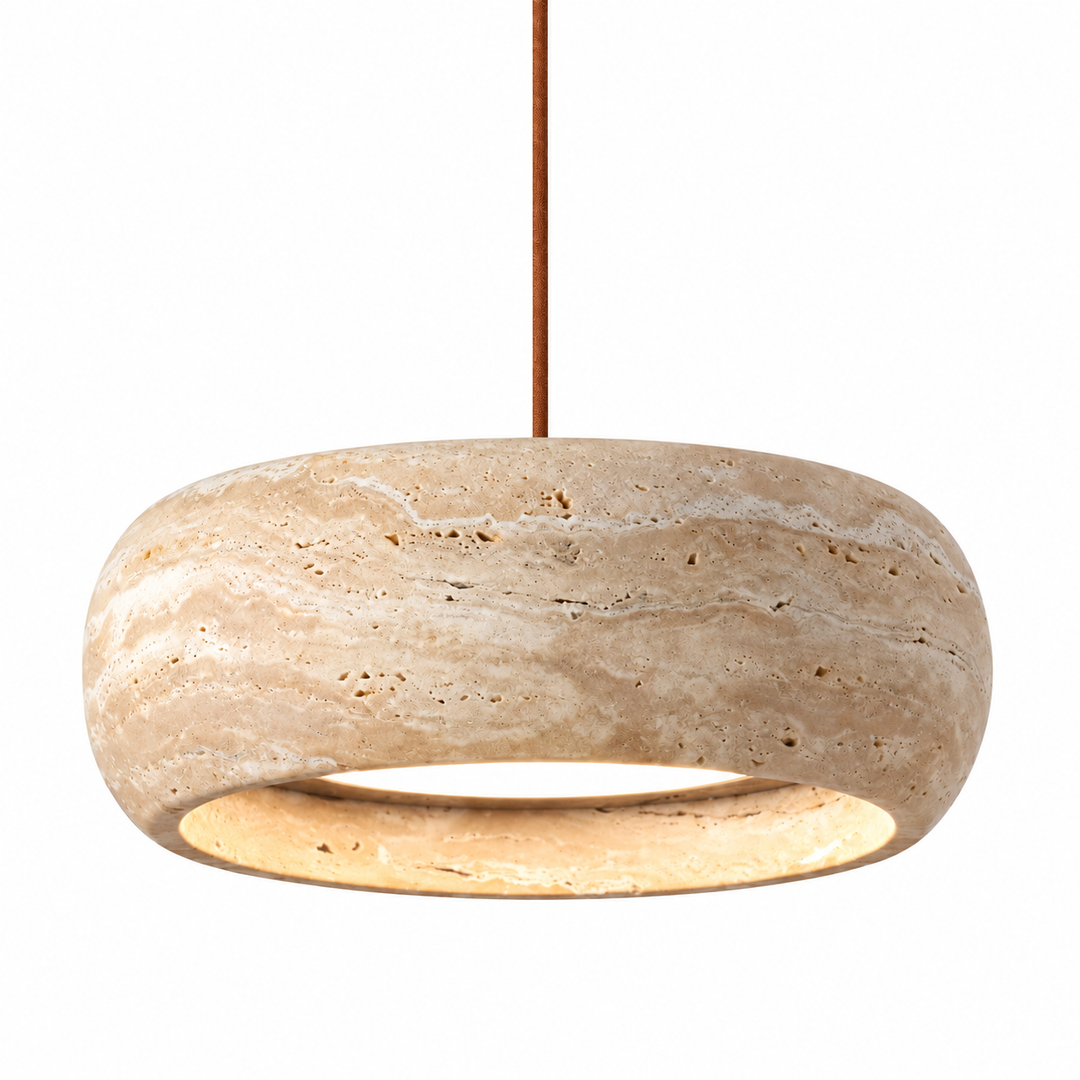 A modern pendant light fixture with a thick, rounded stone disc shade in a natural beige travertine texture, suspended by a slim brown cord against a solid white background.