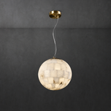 A spherical pendant light made of warm-toned stone or shell-like segments, suspended from a round gold ceiling canopy against a dark charcoal wall.