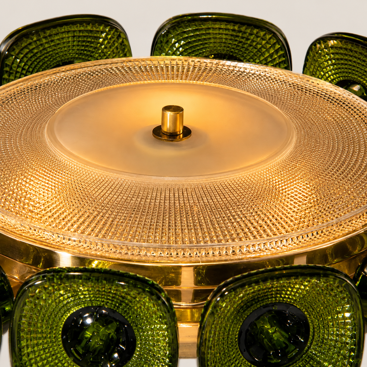 Close-up of the illuminated chandelier showing its textured glass bowl, brass-toned frame and surrounding green glass panels.