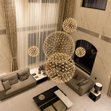 Globe pendant light grouping with glowing geometric metal frames hangs above gray sofas in a double-height living room.