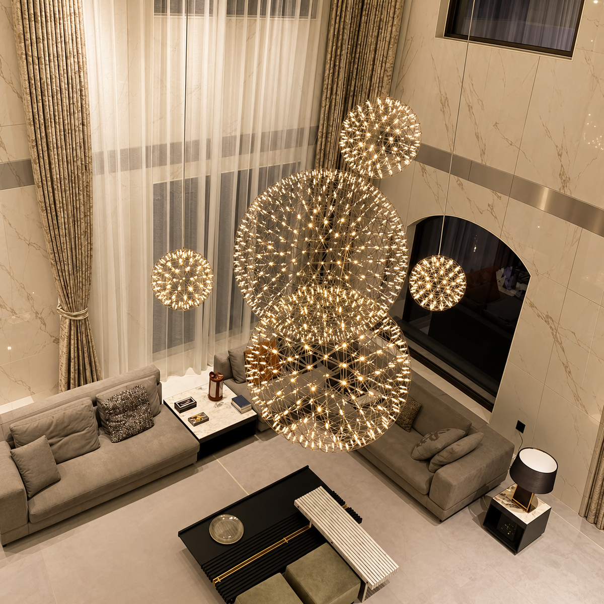 Globe pendant light grouping with glowing geometric metal frames hangs above gray sofas in a double-height living room.