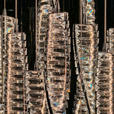 A close-up of a modern chandelier with multiple vertical clusters of clear faceted glass blocks and prisms, suspended by thin metal rods against a dark background. The transparent glass pieces catch and reflect warm light, creating bright rainbow reflections.
