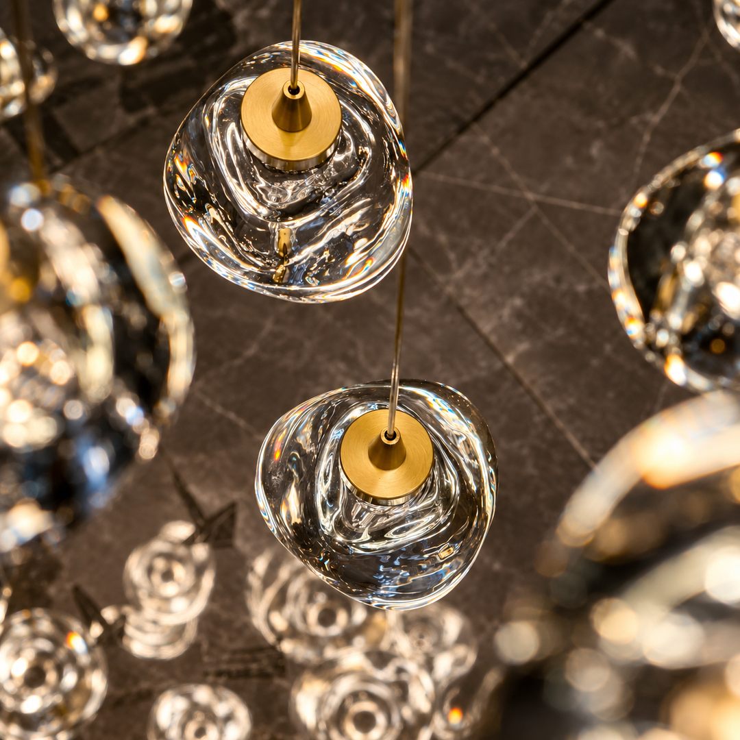 Chandelier detail showing cascading clear crystal drops with gold-toned caps against a dark stone background.