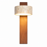 A modern wall sconce featuring a tall, rectangular warm brown wood base, a cylindrical textured beige stone shade, and a dark brown wood mounting plate, shown illuminated against a solid white background.
