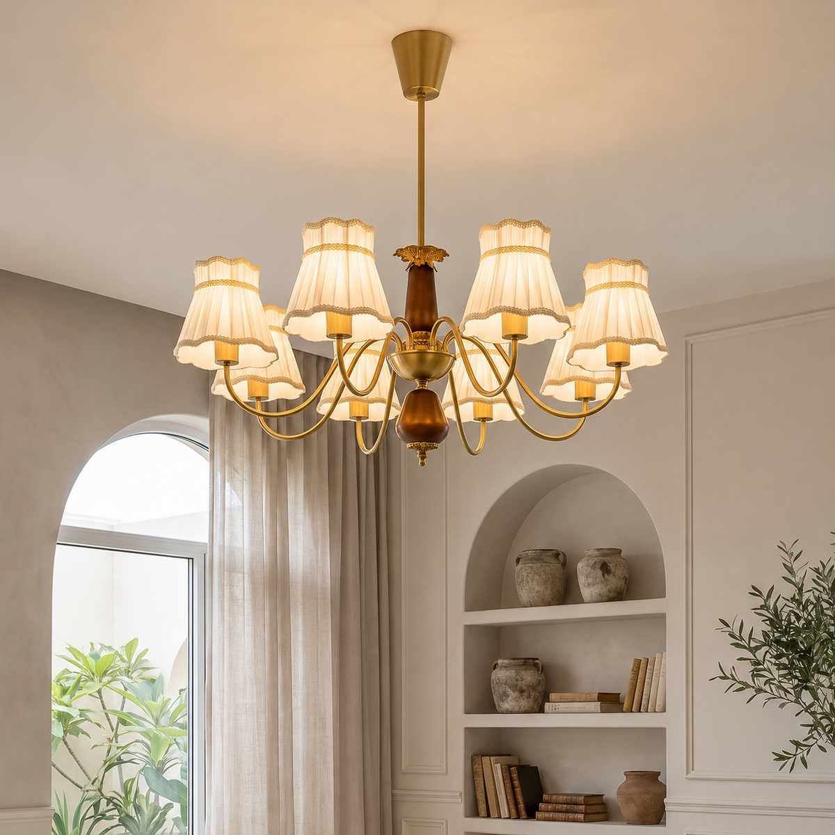 A multi-arm brass chandelier with cream fabric drum shades hangs in a warm, elegant room with built-in shelves, arched windows, and neutral-toned decor.