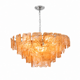 A modern chandelier with a tiered, wavy amber-orange glass shade suspended from a silver-toned chain and ceiling canopy, shown against a plain white background.