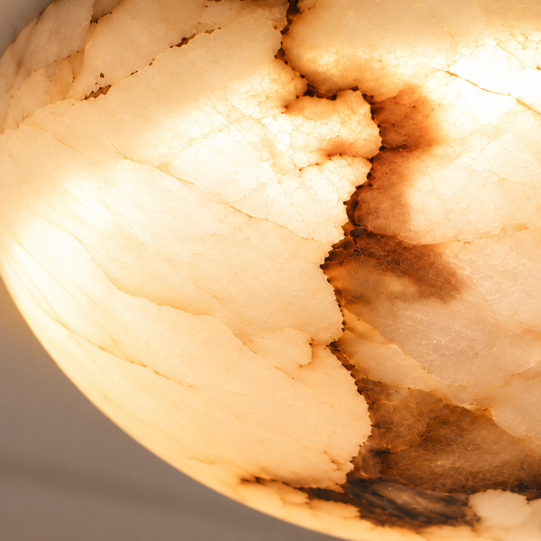 Close-up of the illuminated alabaster ceiling light showing cream and amber tones with dark natural veining against a gray background.