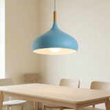 A modern blue pendant light with a warm wood accent and glowing bulb, hanging above a light wood dining table in a minimalist room.