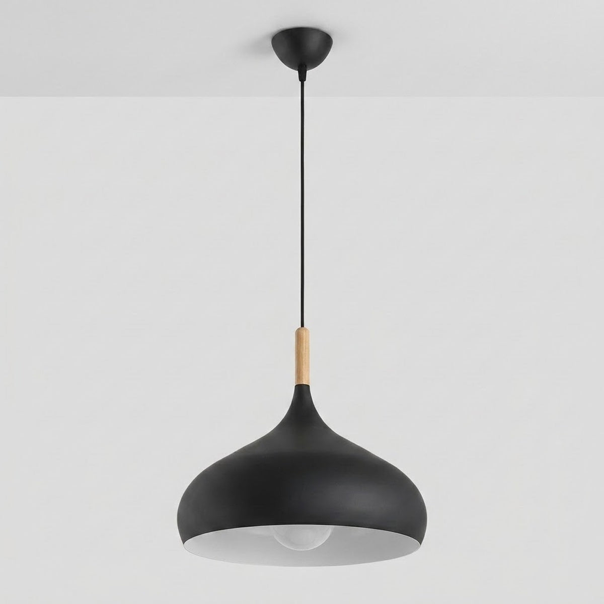 A modern black pendant light with a conical shade, a light wood accent near the top, and a black cord hanging from a ceiling mount against a white wall.