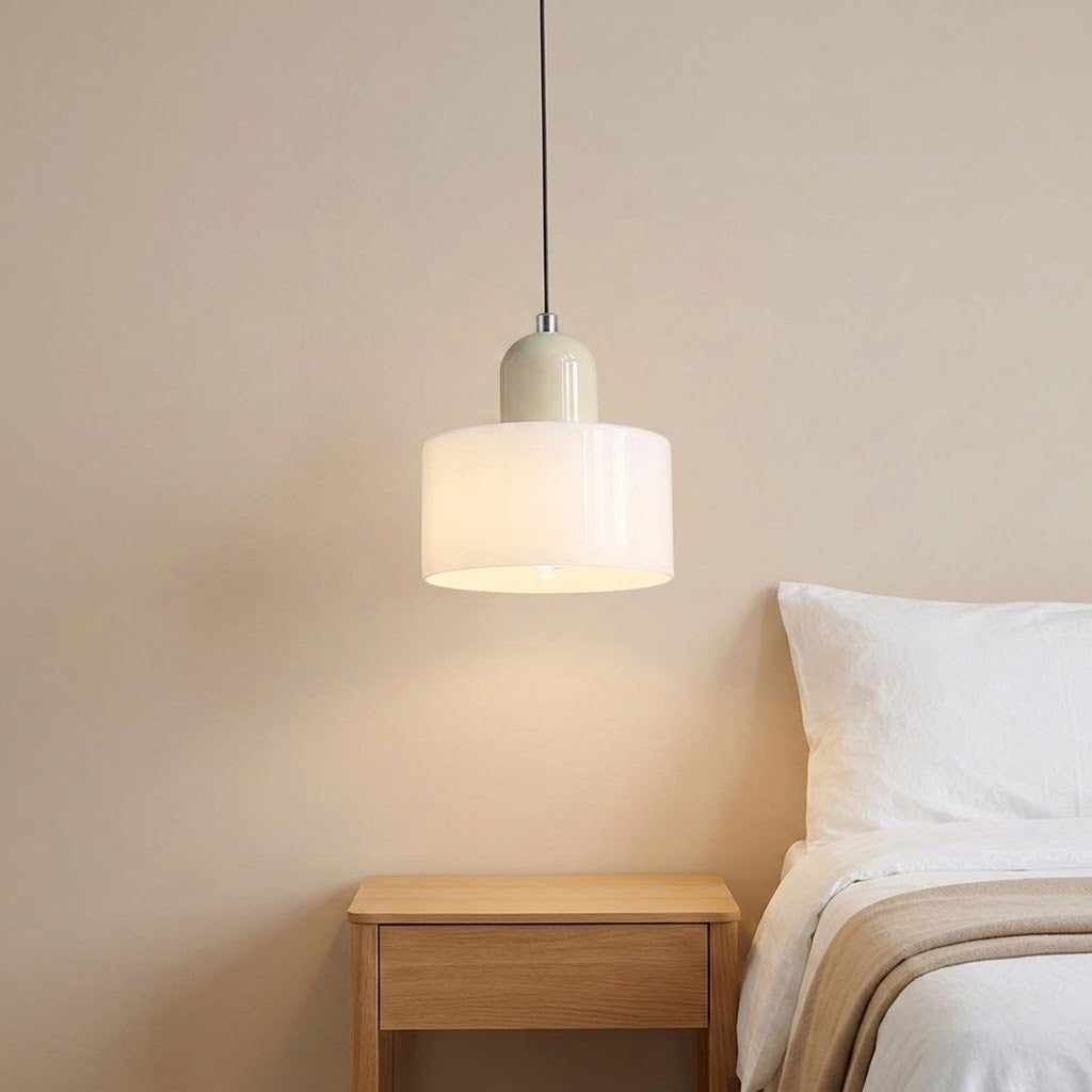 A white glass chandelier with a pale beige rounded top hangs above a wooden bedside table beside white bedding.