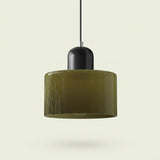 A chandelier with an olive-green cylindrical glass shade and rounded black top hangs from a black cord against a pale background.