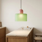 A glowing light green glass chandelier with a pink top hangs above a pale countertop and wooden kitchen island.