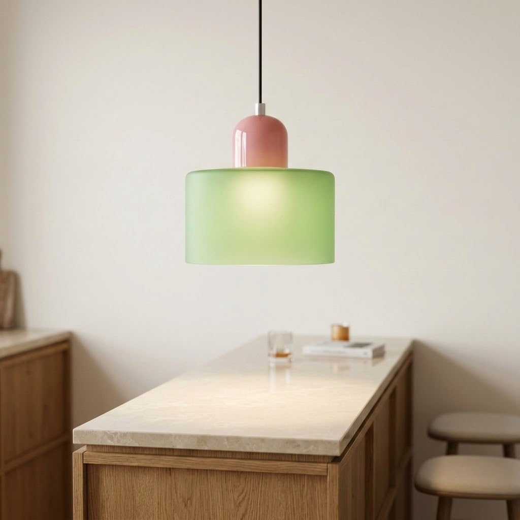A glowing light green glass chandelier with a pink top hangs above a pale countertop and wooden kitchen island.