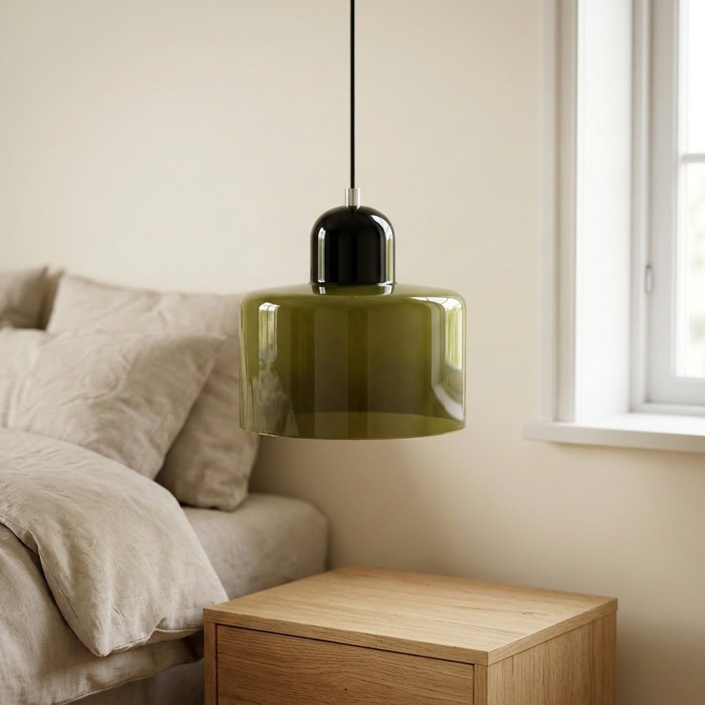 An olive green glass chandelier with a glossy dark cap hangs above a wooden nightstand beside a bed and window.