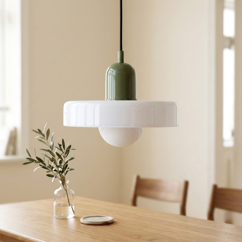 A modern pendant light with a white flared shade, a white globe bulb, and an olive green cylindrical top, hanging over a wooden dining table in a softly lit room.