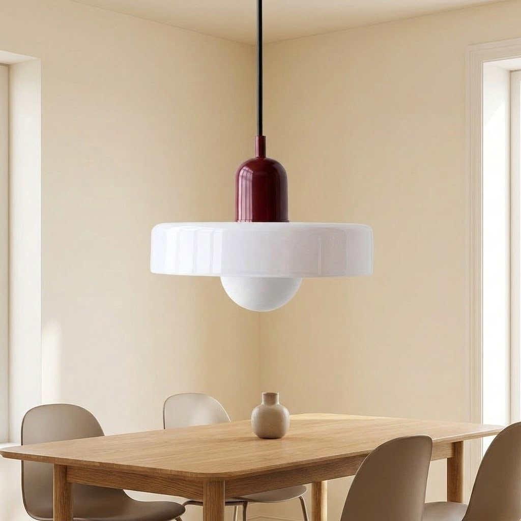 A modern pendant light with a glossy white circular shade and a dark burgundy cylindrical top, hanging in a dining room above a wooden table with chairs.