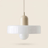 A modern pendant light with a matte beige cylindrical neck, a wide white translucent horizontal shade, and a white globe bulb underneath, suspended against a solid beige background.