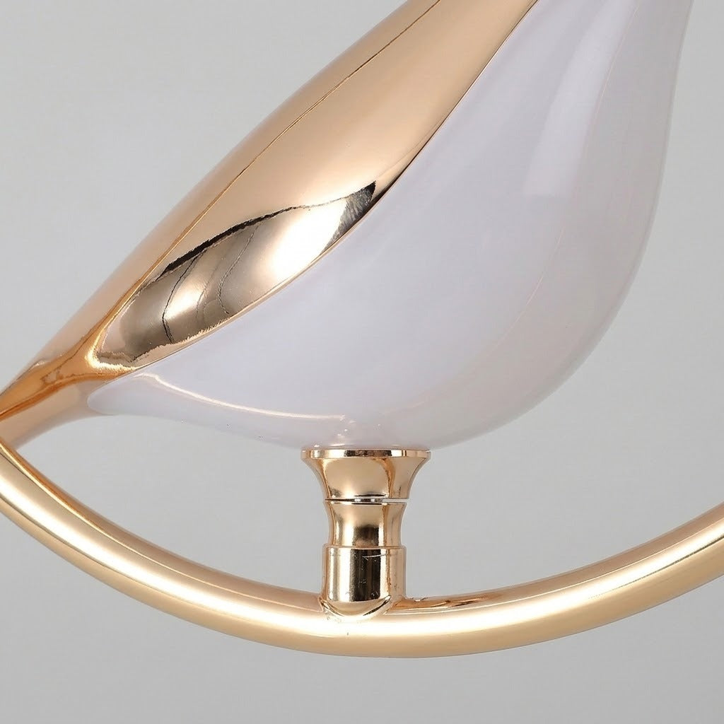 Close-up of a pendant light showing its glossy white bird-shaped shade, reflective gold-toned detailing and curved frame against a gray background.