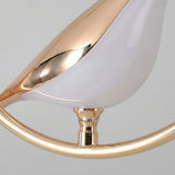 Close-up of a pendant light showing its glossy white bird-shaped shade, reflective gold-toned detailing and curved frame against a gray background.