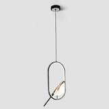 A modern pendant light fixture with a black circular ceiling canopy, a thin black suspension cord, and an elongated oval frame. The frame contains a warm gold-toned leaf-shaped light diffuser, casting a soft glow against a clean, light gray background.