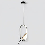 A modern pendant light fixture with a black circular ceiling canopy, a thin black suspension cord, and a geometric oval frame. Inside the frame, a warm-toned geometric shade or leaf-like element glows with a white diffuser, set against a plain light gray background.