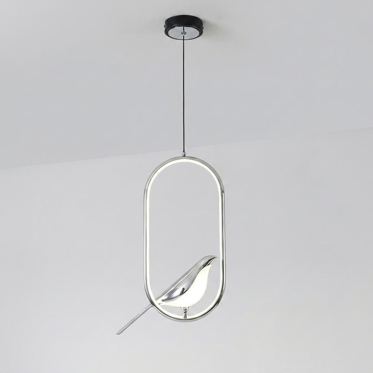 A modern pendant light fixture with a polished chrome oval frame and a sculptural bird-shaped shade, suspended by a thin cord from a black ceiling canopy against a plain white ceiling.