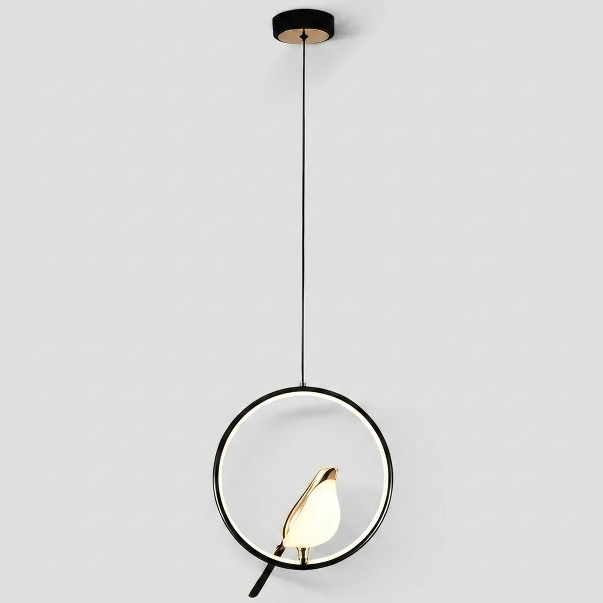 Modern pendant light with a black circular frame, black cord, and a small gold bird-shaped shade holding a glowing white bulb, shown against a light gray background.