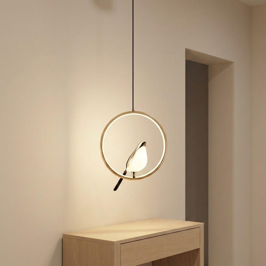A modern pendant light with a circular gold frame and a bird-shaped bulb, hanging above a light wood console table in a minimalist room.