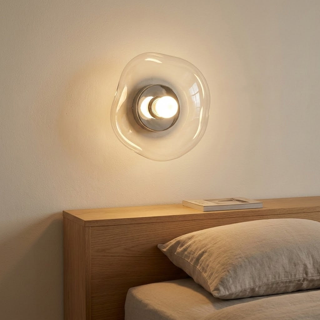Clear glass wall sconce with a silver center casts warm light above a wooden headboard and neutral bedding.