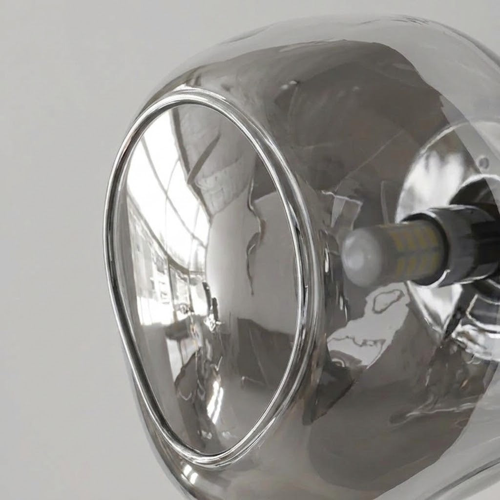 Close-up of a wall sconce showing its curved reflective glass shade, smooth edge, silver socket, and exposed bulb.