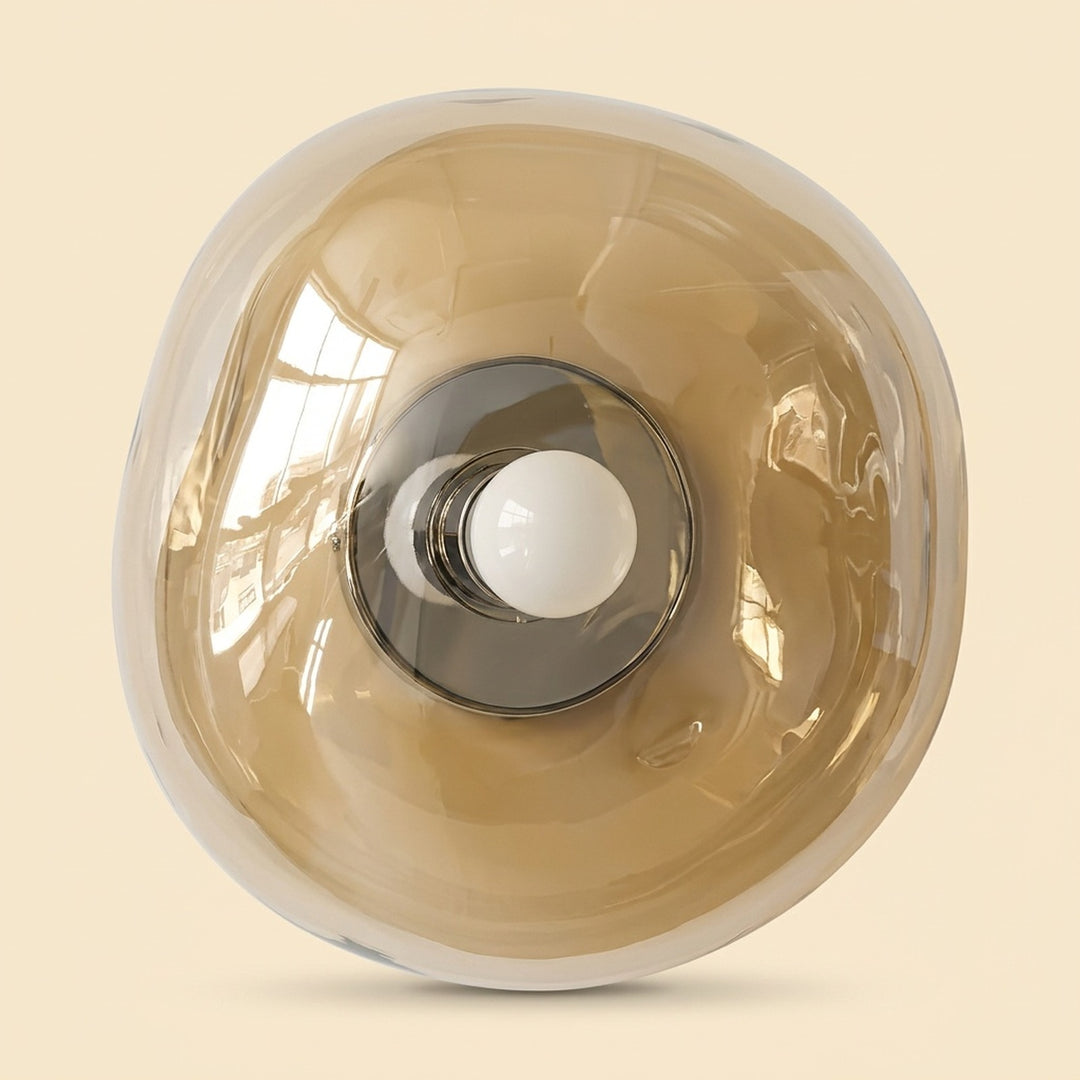 Amber glass wall sconce with an irregular rounded shade, central white bulb and silver fitting against a cream background.