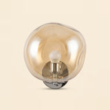 Amber glass wall sconce with an uneven rounded shade, visible upright bulb and polished silver base against a cream background.