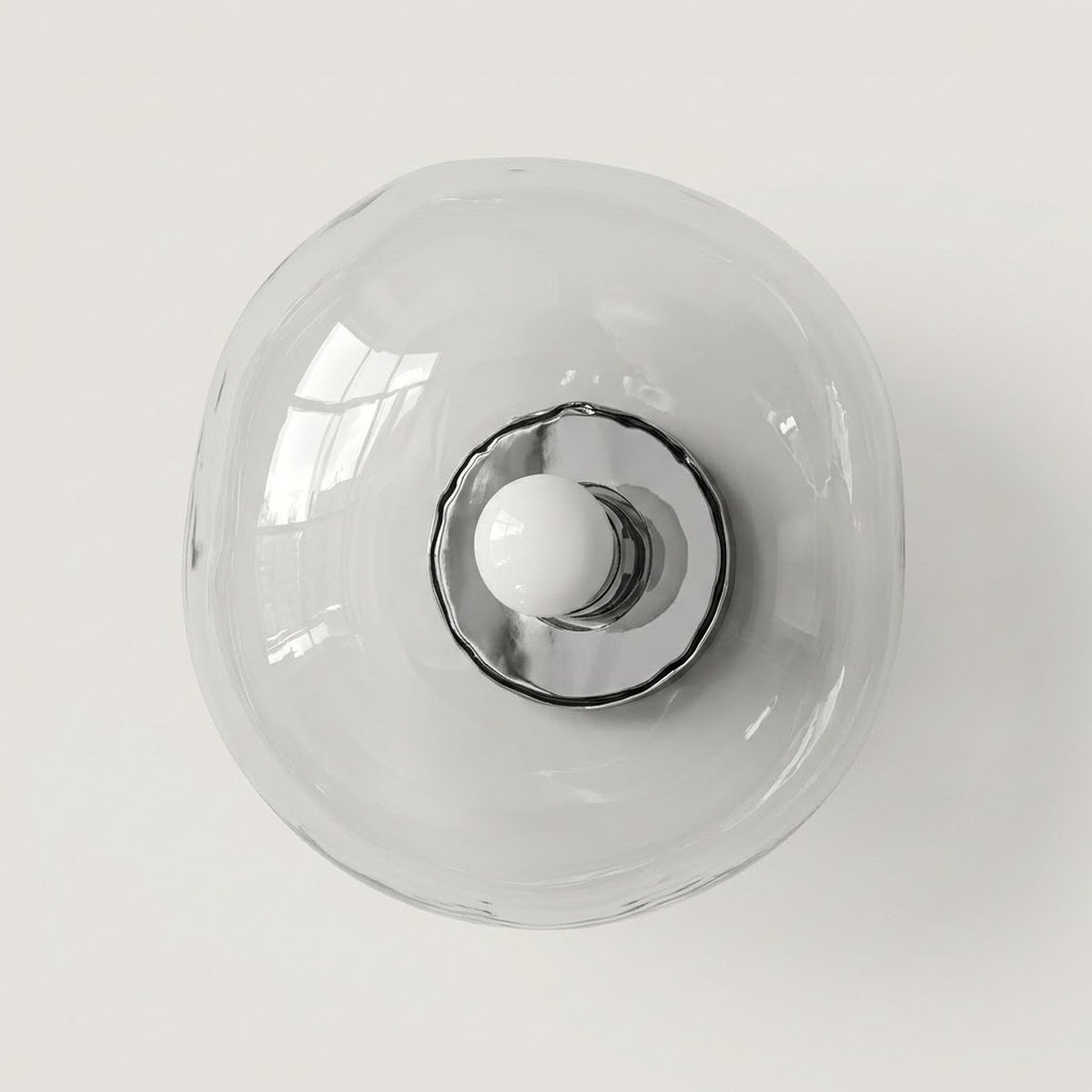 Clear glass wall sconce with an irregular rounded shade, polished silver center, and white bulb against a light neutral background.