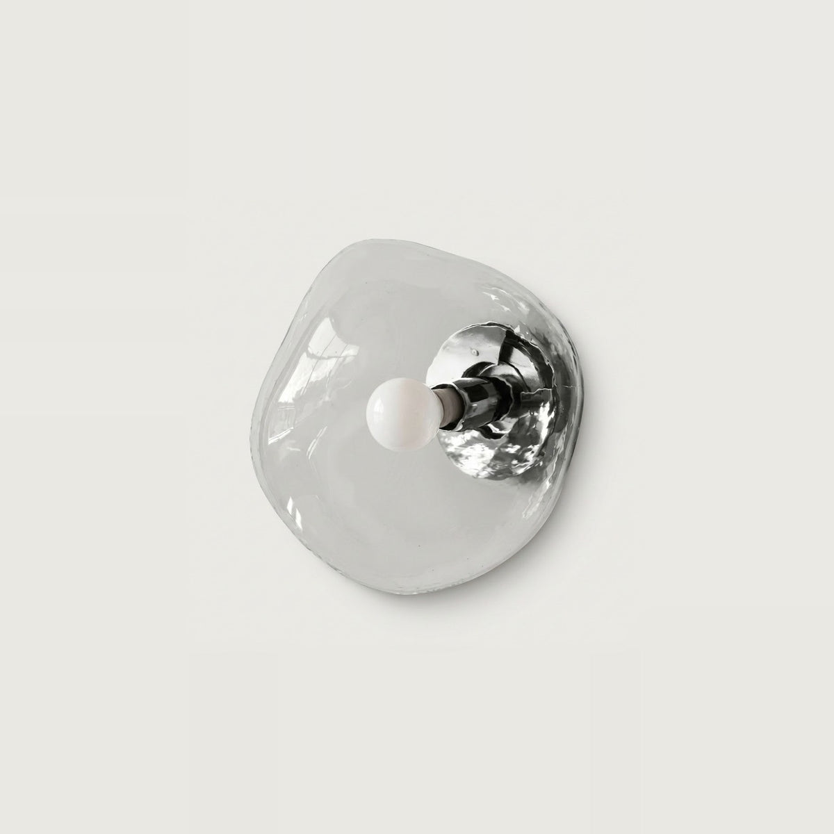 An organic-shaped, translucent clear glass wall sconce with a polished silver metal backplate and a small white spherical bulb, shown against a solid light gray background.