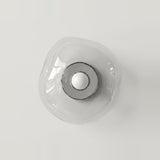Clear glass wall sconce viewed from the front, with a circular silver center and white bulb against a pale background.