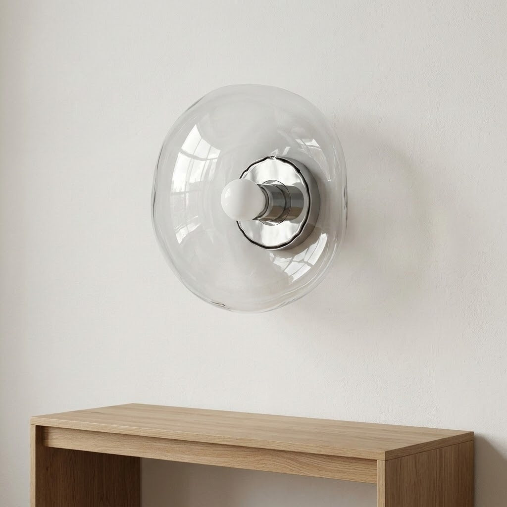 Clear glass wall sconce with a silver socket is mounted on a white wall above a wooden console.