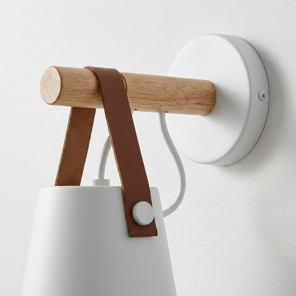 White wall sconce close-up shows a wooden peg, brown straps, round white wall plate and looping white cable.