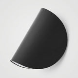 A minimalist black semi-circular wall sconce with a matte finish, shown mounted on a clean white wall.
