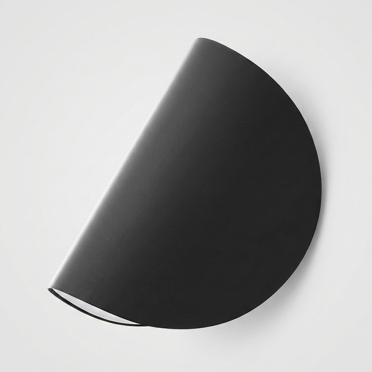 A minimalist black semi-circular wall sconce with a matte finish, shown mounted on a clean white wall.