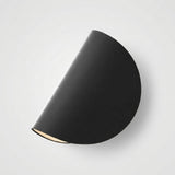 A modern semi-circular wall sconce in matte black, shown from an overhead angle against a light gray background.