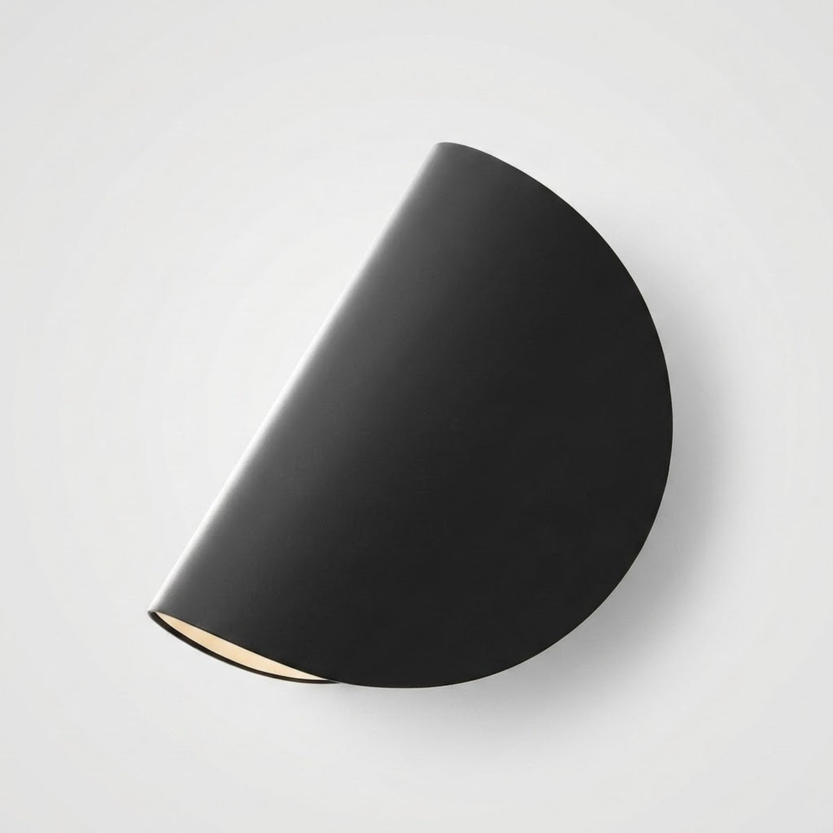 A modern semi-circular wall sconce in matte black, shown from an overhead angle against a light gray background.