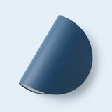 A modern semi-circular wall sconce in a matte slate blue finish, shown from an angle against a clean, very light blue background.