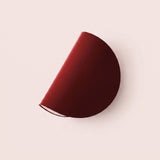 A modern semi-circular wall sconce in a deep burgundy red finish, mounted on a solid pale pink wall.