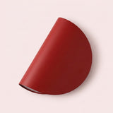A minimalist, semi-circular wall sconce in a matte deep red finish, shown against a solid pale pink background.