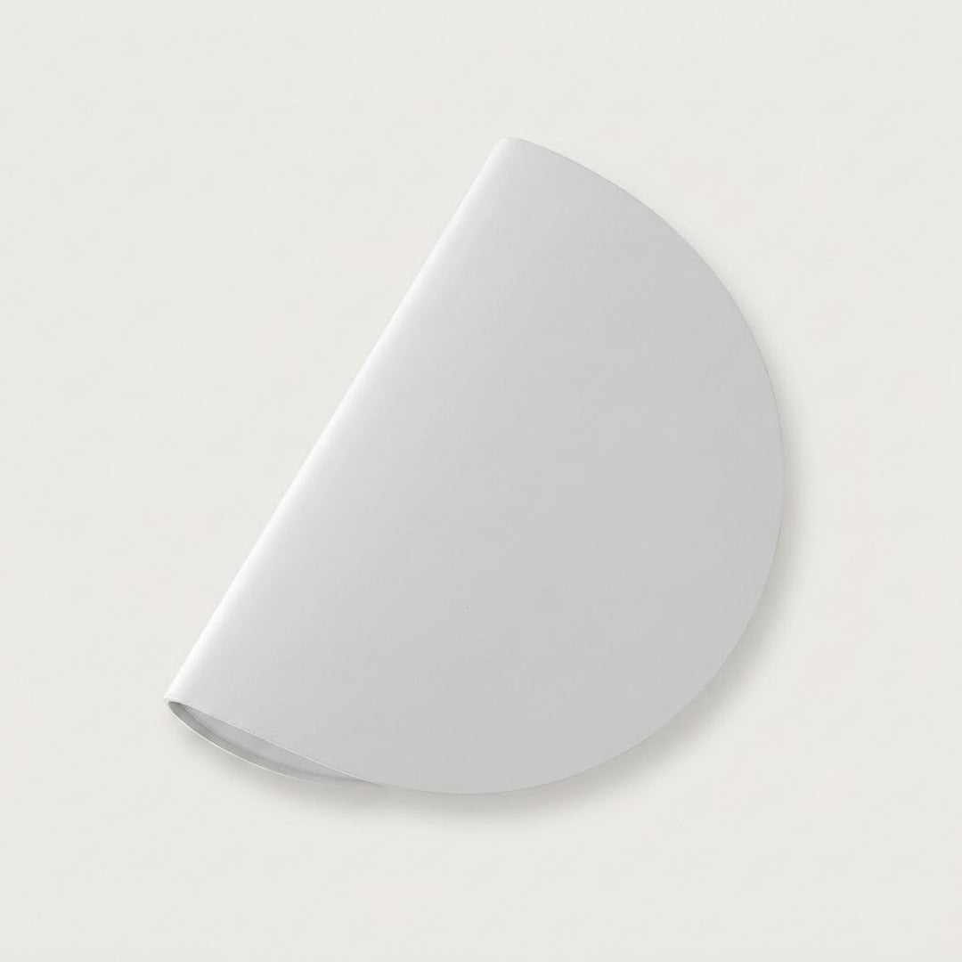 A white wall sconce appears diagonally against an off-white background, showing its semicircular shade and a subtle shadow.